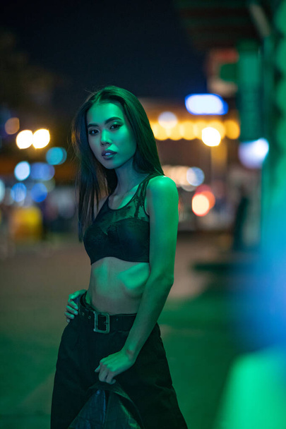 Joven asiático mujer poses en sujetador en noche ciudad contra luces fondo. - Foto, imagen