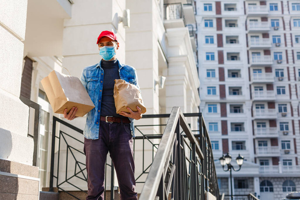 homem de entrega de alimentos com sacos em uma máscara protetora em seu rosto - Foto, Imagem