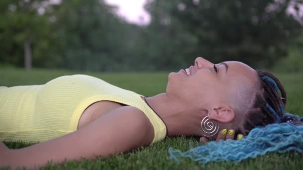 Νεαρή ελκυστική γυναίκα βρίσκεται και ξεκουράζεται στο πάρκο στο πράσινο γρασίδι - Πλάνα, βίντεο