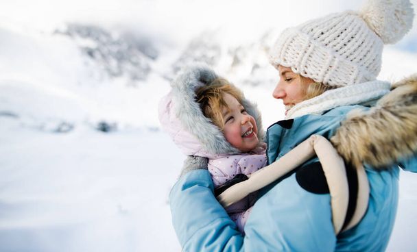 Matka ze szczęśliwą córeczką w nosicielce stojąca w zimowej naturze, odpoczywająca. - Zdjęcie, obraz