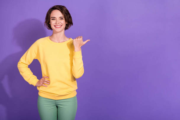Photo of positive girl point thumb finger empty space for ads promotion wear trousers pullover isolated on violet color background - Foto, immagini