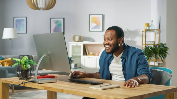 Shocked and Surprised Young Black Man Uses Personal Computer at Home. In the Background Cozy Living Room. - Foto, Bild