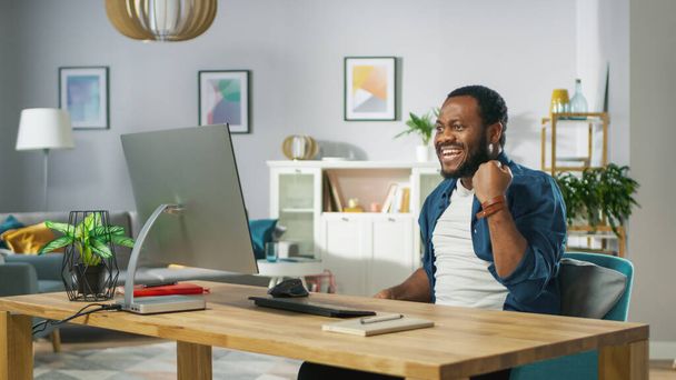 Excited Young Man Uses Personal Computer at Home, Wins Big, Does "Yes" Gesture, Celebrates Victory Emotionally. In the Background Cozy Living Room. - Fotó, kép