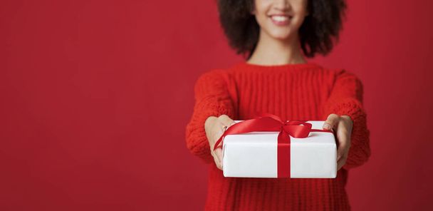 Ritratto di donna afro-americana sorridente in maglione ritagliato in studio dà scatola con regalo - Foto, immagini