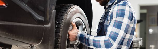 cropped view of mechanic fixing wheel on car, banner - Foto, imagen