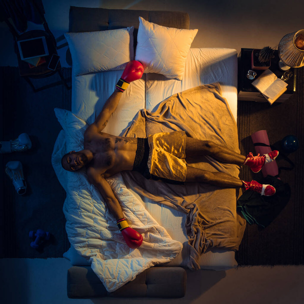 Top view of young professional boxer, fighter sleeping at his bedroom in sportwear with gloves - Φωτογραφία, εικόνα