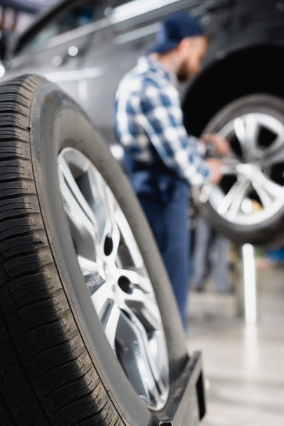 close up view of wheel near mechanic repairing car on blurred background - Foto, Imagen