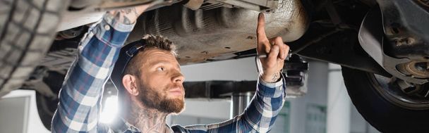mechanic examining bottom of lifted automobile, banner - Foto, afbeelding