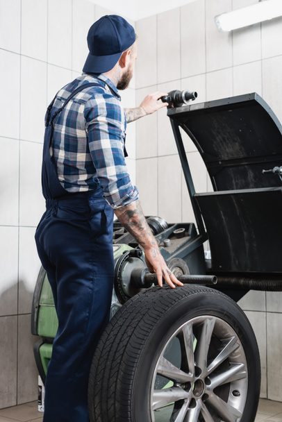 Mechaniker überprüft Rad an Auswuchtmaschine in Werkstatt - Foto, Bild