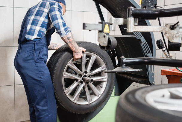 cropped view of technician examining wheel on balance control machine in garage on blurred foreground - Фото, изображение