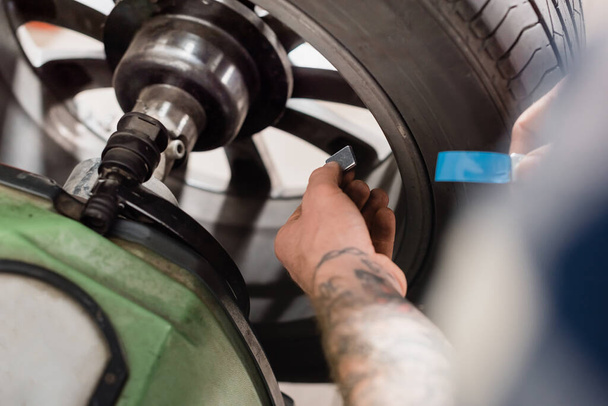 partial view or repairman holding metallic balancing detail near wheel on blurred foreground - Фото, изображение