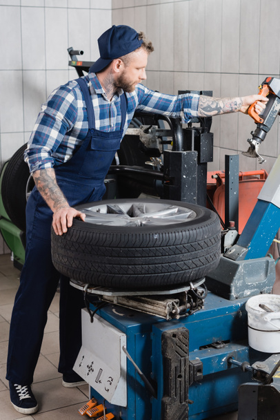 Junger Mechaniker arbeitet in Werkstatt mit Reifenersatzmaschine - Foto, Bild