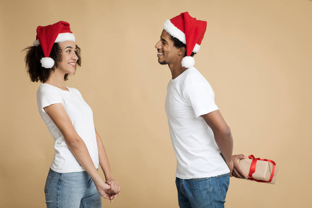 Šťastný mladý pár slaví Nový rok a Vánoce na párty. Afričan Američan v klobouku s úsměvem držení box - Fotografie, Obrázek