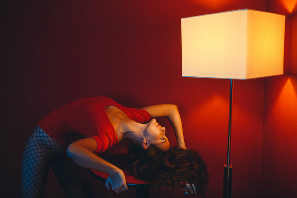 a young girl in a red bodysuit in a room with red walls, around her are two large square lamps - Photo, Image