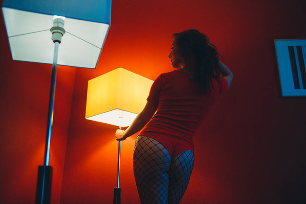 a young girl in a red bodysuit in a room with red walls, around her are two large square lamps - Foto, Bild