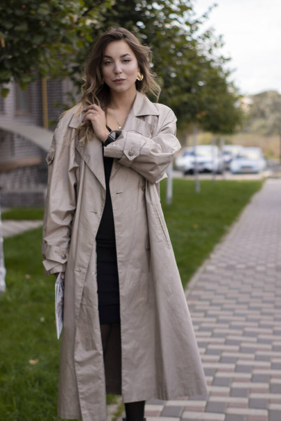 atraktivní štíhlé mladé brunetky v módní trenč kabát a černé šaty s novinami - Fotografie, Obrázek