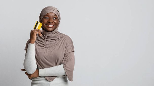 Zamyślona afrykańska muzułmanka w hidżabie trzyma kartę kredytową i odwraca wzrok - Zdjęcie, obraz