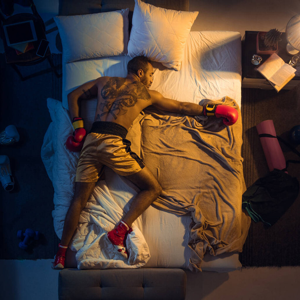Top view of young professional boxer, fighter sleeping at his bedroom in sportwear with gloves - Foto, imagen