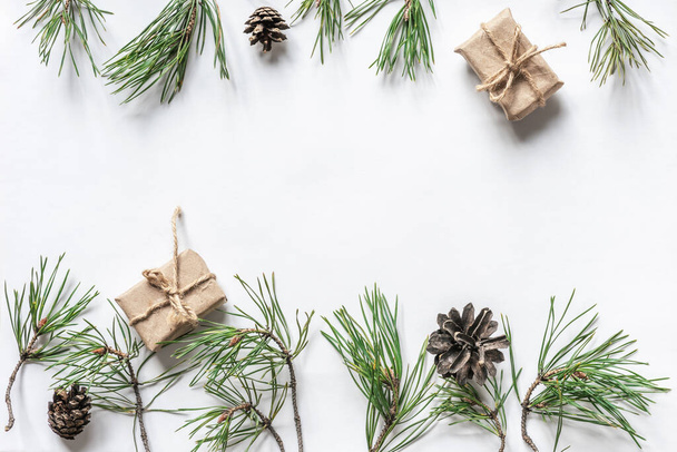 Winter festive background mockup for Christmas or New Year surrounded by natural pine branches, presents and cones on a white backdrop. Top view, copy space. - Photo, Image