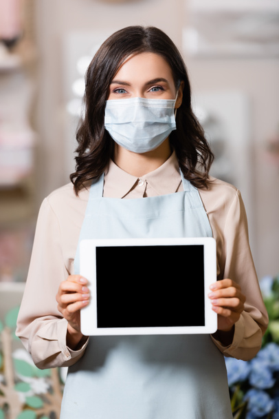 florist in medical mask holding tablet with blank screen while looking at camera - Foto, Imagem