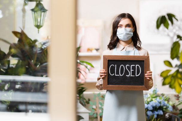 young florist in medical mask holding board with closed lettering on blurred foreground - Photo, Image