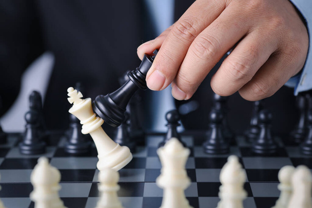 Руки предпринимателя управляют шахматным королем до успешной позиции на конкурентной бизнес-игре с падением вражеских шахмат, что означает планирование и стратегическое решение и достижение цели. - Фото, изображение