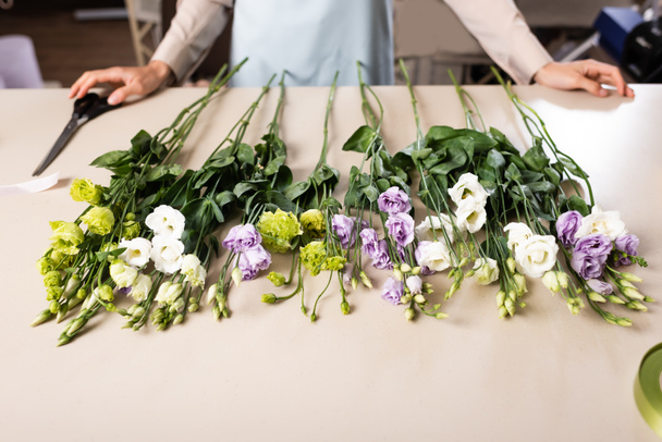 обрезанный вид флориста рядом с цветами эустомы на столе в цветочном магазине на размытом фоне - Фото, изображение