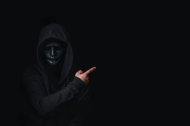 Опасный анонимный хакер в капюшоне и маске взломать данные безопасности и взломать пароль банковским счетом. Он указывает на пустое место для вашего рекламного контента, концепцию безопасности кибератак - Фото, изображение