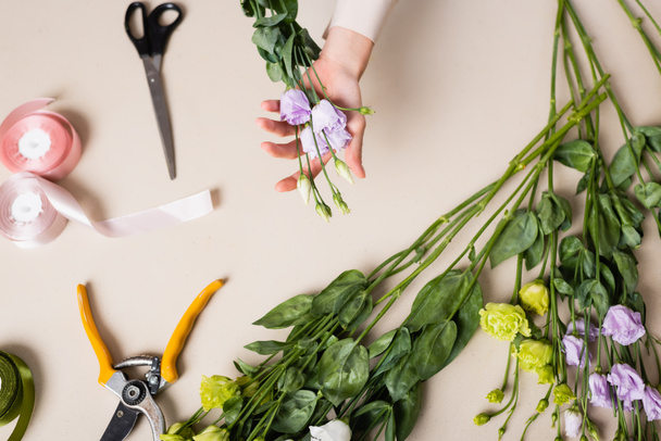 vista dall'alto del fiorista che tiene fiori di eustoma vicino a forbici, forbici e nastro decorativo mentre fa bouquet - Foto, immagini