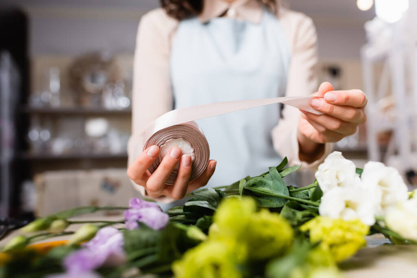 cropped view of florist holding decorative ribbon near eustoma flowers while making bouquet on blurred foreground - Фото, зображення