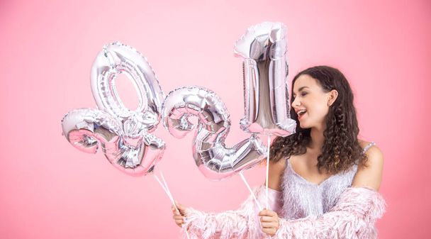 Attraente ragazza gioiosa su uno sfondo rosa con palloncini d'argento dai numeri 2021 nelle sue mani. Il concetto di celebrazione di Capodanno - Foto, immagini