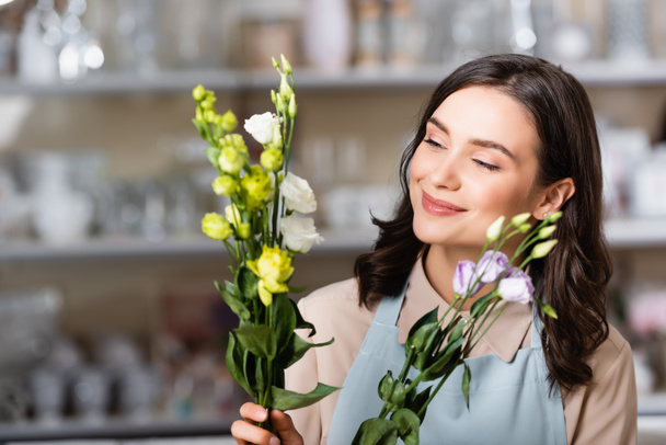 cheerful florist holding eustoma flowers in flower shop on blurred background - Foto, immagini