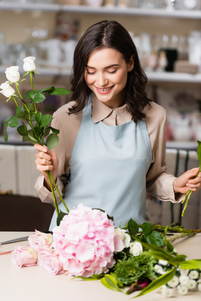 Happy naaras kukkakauppias ruusut katselee kukkia pöydällä, kun säveltäminen kimppu hämärtynyt tausta - Valokuva, kuva