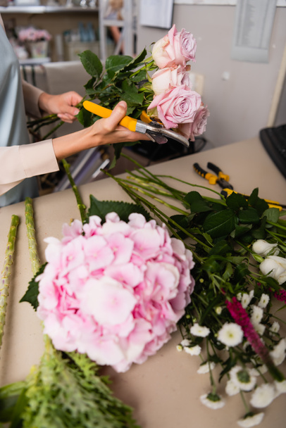Vágott kilátás virágárus metszőollóval és rózsával az íróasztal mellett, homályos virágokkal az előtérben - Fotó, kép
