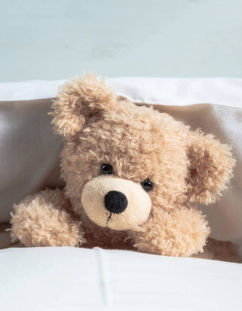 Children bedtime. Cute teddy laying on bed mattress playing with pillows - Photo, Image