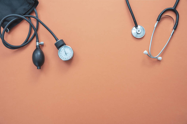 Vybavení pro měření krevního tlaku, kontrola hypertenze. Lékařský stetoskop a sfygmomanometr na pastelově oranžové barvy pozadí, horní pohled. - Fotografie, Obrázek