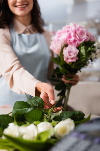 Kadın çiçekçinin masadan gül alırken arka planda bulanık bir buket bestelediği görüntüler. - Fotoğraf, Görsel