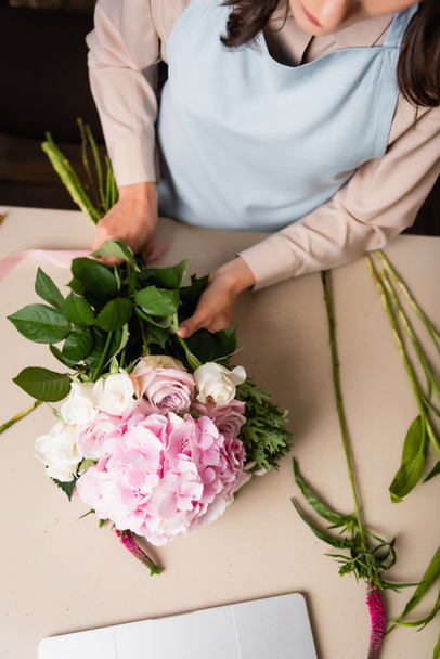 Vista cortada de florista feminino em avental compondo buquê na mesa com talos - Foto, Imagem