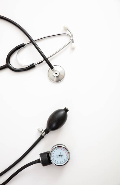 Blutdruckmessgeräte, Hypertoniekontrolle. Medizinisches Stethoskop und Blutdruckmessgerät auf weißem Hintergrund, Draufsicht. - Foto, Bild