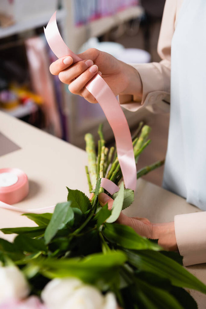 Close-up vista da mão florista segurando fita decorativa, enquanto amarra talos de buquê na loja de flores no fundo borrado - Foto, Imagem
