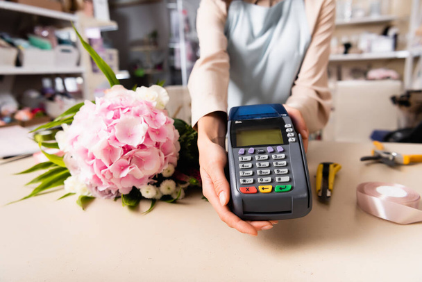 Cropped view of florist holding terminal near fresh bouquet on desk on blurred background - Photo, Image