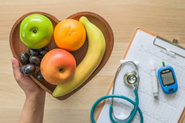 Kolesterol diyeti ve sağlıklı gıda besin konsepti kalp tabağında temiz meyve, beslenme uzmanı izleme, ölçüm aletleri ile kan şekeri kontrol kayıtları  - Fotoğraf, Görsel