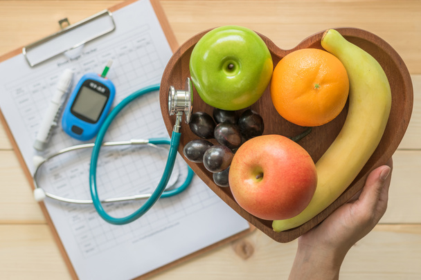 Cholesterol dieet en gezonde voeding concept met schoon fruit in het hart schotel met voedingsdeskundige monitoring, bloedsuiker controle record met meetinstrument kit  - Foto, afbeelding