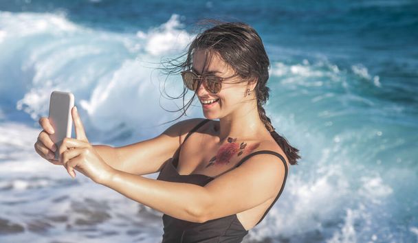 Весела жінка в купальнику бере селфі на тлі морських хвиль
. - Фото, зображення