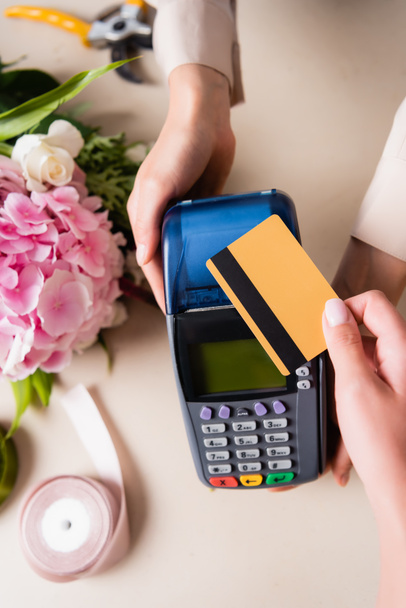 Vista recortada del cliente pagando con tarjeta de crédito por terminal en manos de florista cerca de hortensias florecientes en el escritorio - Foto, imagen