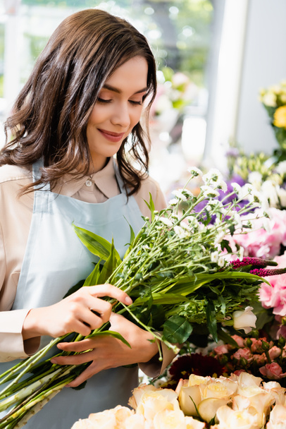 Uśmiechnięta kobieta kwiaciarnia gospodarstwa bukiet chryzantemy i celozji z niewyraźne kwiaty na tle - Zdjęcie, obraz