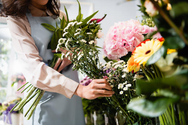 Обрезанный вид флориста, берущего ветку хризантемы, собирающего букет в цветочном магазине на размытом переднем плане - Фото, изображение