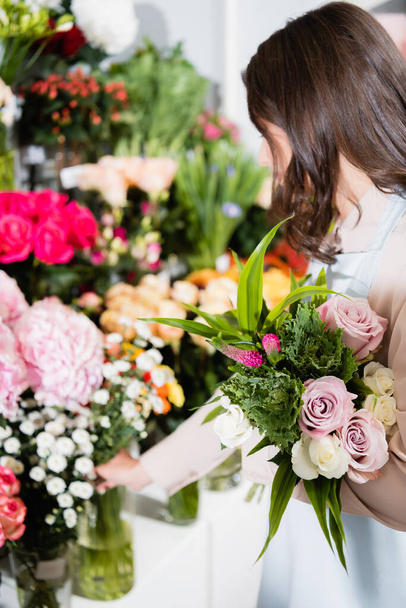 Bruna fiorista femminile con bouquet prendere ramo di crisantemi da rastrelliere di fiori su sfondo sfocato - Foto, immagini