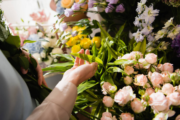 Ausgeschnittene Ansicht des Blumenhändlers mit Blumenstrauß, der sich um Pflanzen in der Nähe von Blumen auf verschwommenem Hintergrund kümmert - Foto, Bild