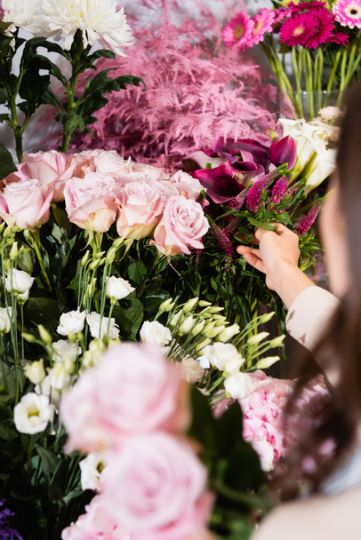 Vue recadrée du fleuriste femelle prenant la celosie à partir d'un porte-fleurs avec des roses floues au premier plan - Photo, image